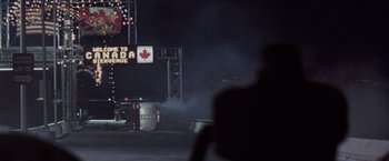 Movie still from “The Long Kiss Goodnight” (1996), directed by Renny Harlin – A man standing in front of a street sign at night; Extreme Wide shot, Low angle