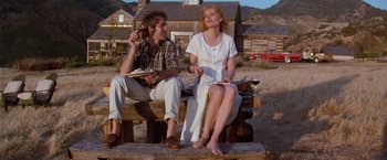 Movie still from “The Long Kiss Goodnight” (1996), directed by Renny Harlin – A man and a woman sitting on a wooden bench; Medium shot, Low angle