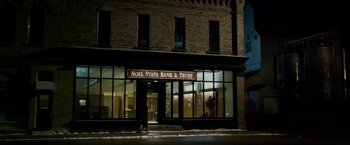 Movie still from “The Lookout” (2007), directed by Scott Frank – A person walking in front of a bank and trust building at night; Extreme Wide shot, Low angle