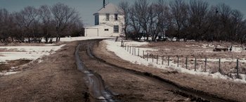 Movie still from “The Lookout” (2007), directed by Scott Frank – A dirt road going through a field next to a house; Extreme Wide shot, High angle