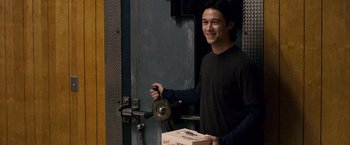 Movie still from “The Lookout” (2007), directed by Scott Frank – A young man holding a pizza box while standing in front of a door; Medium shot, High angle