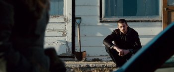 Movie still from “The Lookout” (2007), directed by Scott Frank – A man sitting in front of a building with a shovel; Medium shot, Over the shoulder angle