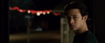 Movie still from “The Lookout” (2007), directed by Scott Frank – A young man is standing in the dark with lights in the background; Close Up shot, Over the shoulder angle