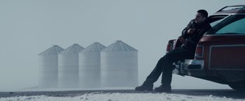 Movie still from “The Lookout” (2007), directed by Scott Frank – A person sitting on the ground in front of some silos; Wide shot, Low angle