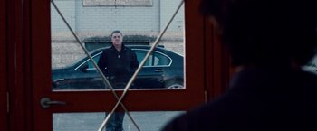 Movie still from “The Lookout” (2007), directed by Scott Frank – A man standing in front of a car looking in a mirror; Wide shot, Over the shoulder angle