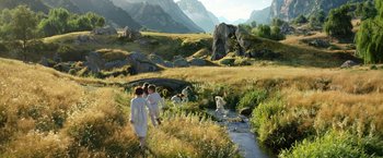Movie still from “The Lord of the Rings: The Rings of Power” (2022), created by Patrick McKay – A group of people walking across a lush green field; Wide shot, High angle