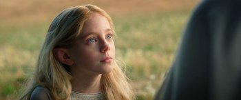 Movie still from “The Lord of the Rings: The Rings of Power” (2022), created by Patrick McKay – A young girl with long blonde hair and blue eyes looking off into the distance; Close Up shot, Over the shoulder angle