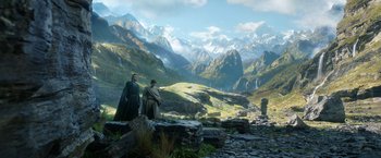 Movie still from “The Lord of the Rings: The Rings of Power” (2022), created by Patrick McKay – Two people standing on a rocky hillside with mountains in the background; Wide shot, Low angle