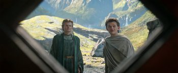 Movie still from “The Lord of the Rings: The Rings of Power” (2022), created by Patrick McKay – Two people standing next to each other near a mountain; Medium shot, Low angle