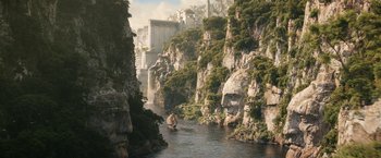 Movie still from “The Lord of the Rings: The Rings of Power” (2022), created by Patrick McKay – A boat traveling down a river surrounded by mountains; Extreme Wide shot, High angle