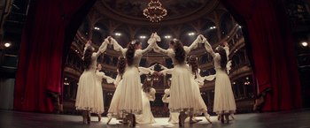 Movie still from “Red Sparrow” (2018), directed by Francis Lawrence – A group of women in white dresses dancing in front of a large audience; Wide shot, High angle