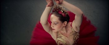 Movie still from “Red Sparrow” (2018), directed by Francis Lawrence – A woman in a red and gold dress holding her arms in the air; Close Up shot, Low angle