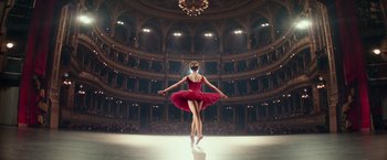 Movie still from “Red Sparrow” (2018), directed by Francis Lawrence – A woman in a red dress standing on one leg in front of an audience; Wide shot, Low angle