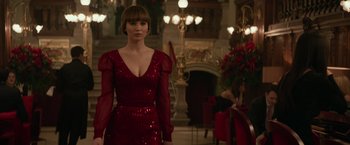 Movie still from “Red Sparrow” (2018), directed by Francis Lawrence – A woman in a red dress standing in front of a fireplace; Medium shot, Over the shoulder angle