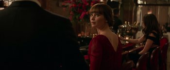 Movie still from “Red Sparrow” (2018), directed by Francis Lawrence – A woman in a red dress is standing in front of a bar; Medium shot, Over the shoulder angle