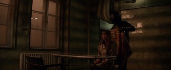 Movie still from “Red Sparrow” (2018), directed by Francis Lawrence – A woman sitting at a table in front of a window; Wide shot, High angle