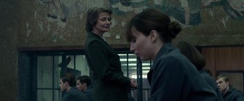 Movie still from “Red Sparrow” (2018), directed by Francis Lawrence – A woman standing next to another woman in a room; Medium shot, Over the shoulder angle