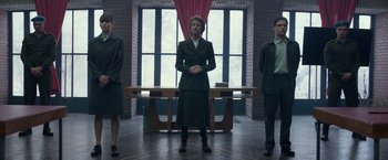 Movie still from “Red Sparrow” (2018), directed by Francis Lawrence – A woman standing in front of two other men in front of a table; Wide shot, Low angle