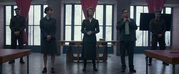 Movie still from “Red Sparrow” (2018), directed by Francis Lawrence – Three people standing in front of a table in front of a window; Medium shot, Low angle