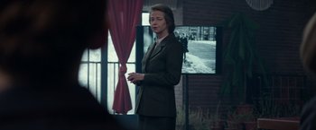 Movie still from “Red Sparrow” (2018), directed by Francis Lawrence – A woman in a suit standing in front of a tv; Medium shot, Over the shoulder angle