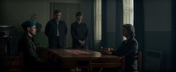 Movie still from “Red Sparrow” (2018), directed by Francis Lawrence – Three people standing around a table in a room; Medium shot, Low angle