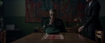 Movie still from “Red Sparrow” (2018), directed by Francis Lawrence – A man sitting at a wooden table with his hand to his face; Medium shot, Over the shoulder angle