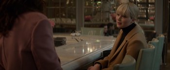 Movie still from “Red Sparrow” (2018), directed by Francis Lawrence – A woman sitting at a table in front of other people; Medium shot, Over the shoulder angle