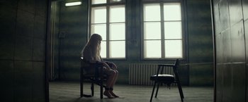 Movie still from “Red Sparrow” (2018), directed by Francis Lawrence – A woman sitting on a chair in a room with two windows; Wide shot, High angle