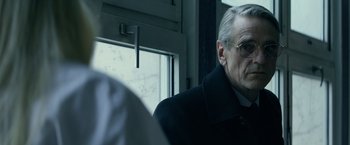 Movie still from “Red Sparrow” (2018), directed by Francis Lawrence – An older man wearing glasses and a black coat; Close Up shot, Low angle