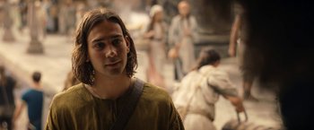 Movie still from “The Lord of the Rings: The Rings of Power” (2022), created by Patrick McKay – A man in a brown shirt is standing in front of a group of people; Close Up shot, Over the shoulder angle