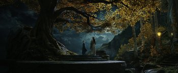 Movie still from “The Lord of the Rings: The Rings of Power” (2022), created by Patrick McKay – Two people standing on steps in front of a large tree; Wide shot, Low angle