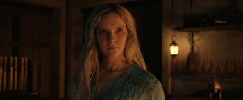 Movie still from “The Lord of the Rings: The Rings of Power” (2022), created by Patrick McKay – A woman with long blonde hair standing in a dark room; Close Up shot, Over the shoulder angle