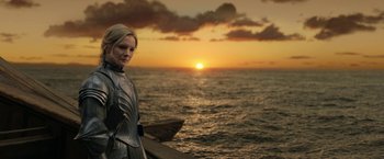 Movie still from “The Lord of the Rings: The Rings of Power” (2022), created by Patrick McKay – A woman standing in front of a body of water at sunset; Medium shot, Low angle