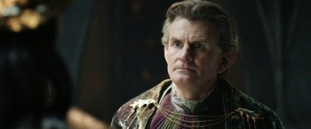 Movie still from “The Lord of the Rings: The Rings of Power” (2022), created by Patrick McKay – An older man wearing a colorful outfit and looking at the camera; Close Up shot, Over the shoulder angle