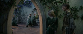 Movie still from “The Lord of the Rings: The Rings of Power” (2022), created by Patrick McKay – A woman in a green dress standing in front of a building; Wide shot, Over the shoulder angle