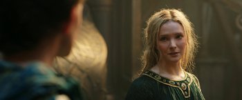 Movie still from “The Lord of the Rings: The Rings of Power” (2022), created by Patrick McKay – A woman in a green and gold dress looking into the camera; Close Up shot, Over the shoulder angle