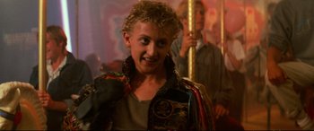 Movie still from “The Lost Boys” (1987), directed by Joel Schumacher – A young man with blonde curly hair wearing a colorful jacket; Close Up shot, Low angle