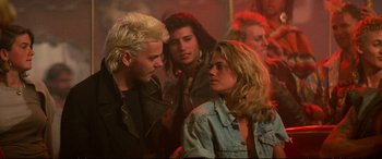 Movie still from “The Lost Boys” (1987), directed by Joel Schumacher – A group of people standing around each other in a room; Medium shot, Over the shoulder angle