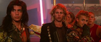Movie still from “The Lost Boys” (1987), directed by Joel Schumacher – A man with long blonde hair is wearing a black jacket; Medium shot, Over the shoulder angle