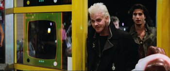 Movie still from “The Lost Boys” (1987), directed by Joel Schumacher – A man with white spiky hair standing next to a bus; Medium shot, Over the shoulder angle