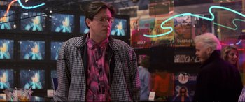 Movie still from “The Lost Boys” (1987), directed by Joel Schumacher – A man in a plaid jacket standing next to a neon sign; Medium shot, Over the shoulder angle