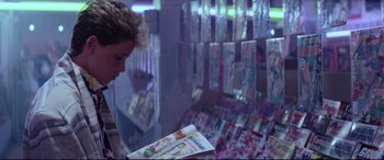 Movie still from “The Lost Boys” (1987), directed by Joel Schumacher – A woman looking at a comic book in a store window; Medium shot, Over the shoulder angle
