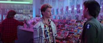 Movie still from “The Lost Boys” (1987), directed by Joel Schumacher – A young man standing in front of a display of magazines; Medium shot, Over the shoulder angle