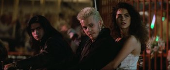 Movie still from “The Lost Boys” (1987), directed by Joel Schumacher – A man with spiky white hair sitting next to other people; Medium shot, Low angle
