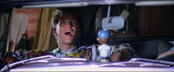 Movie still from “The Lost Boys” (1987), directed by Joel Schumacher – A young man sitting in the driver's seat of a car; Close Up shot, Low angle
