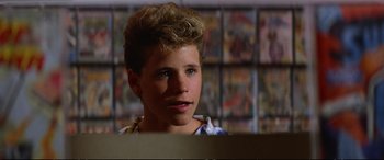 Movie still from “The Lost Boys” (1987), directed by Joel Schumacher – A young man with a blonde hair and blue eyes looking to his left; Close Up shot, Over the shoulder angle