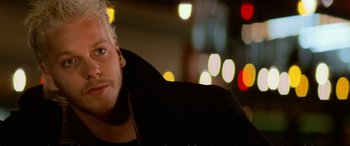 Movie still from “The Lost Boys” (1987), directed by Joel Schumacher – A man with white hair is sitting in front of some lights; Close Up shot, Over the shoulder angle