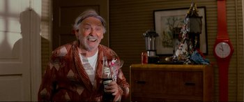 Movie still from “The Lost Boys” (1987), directed by Joel Schumacher – An older man holding a bottle of soda and smiling; Medium shot, Over the shoulder angle