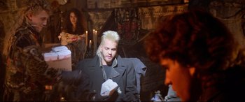 Movie still from “The Lost Boys” (1987), directed by Joel Schumacher – A man with white hair is sitting in a dark room; Medium shot, Over the shoulder angle