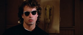 Movie still from “The Lost Boys” (1987), directed by Joel Schumacher – A man wearing sunglasses standing in front of a phone; Close Up shot, Low angle